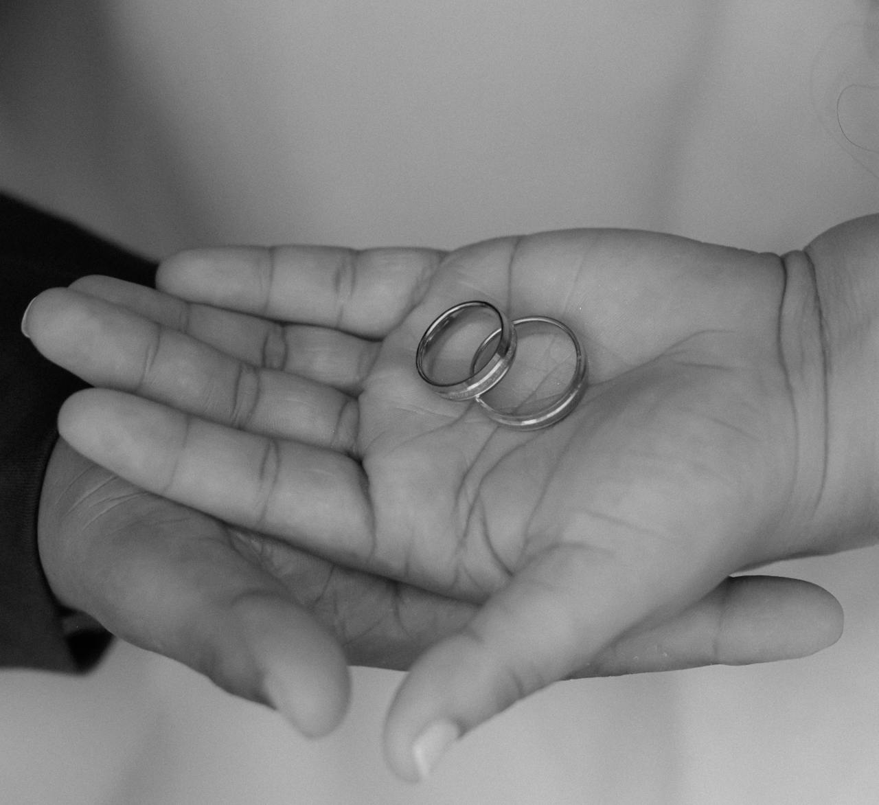 Close-up black and white image of hands holding wedding rings, symbolizing commitment.